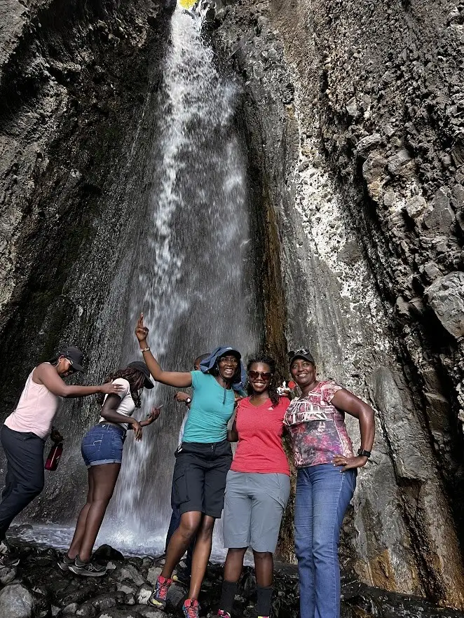Members posing inside the hollow of an enormous tree beside a waterfall